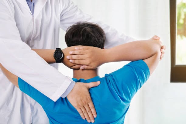 Physical therapist in a white coat performing a back and shoulder adjustment on a seated patient in a blue shirt