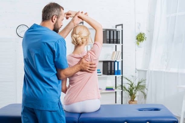 Physical therapist guiding a patient through an arm-raising stretch during a clinical rehabilitation session