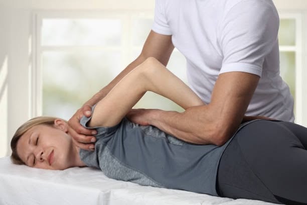 A physical therapist performing a spinal rotation stretch on a woman lying on her side on a treatment table