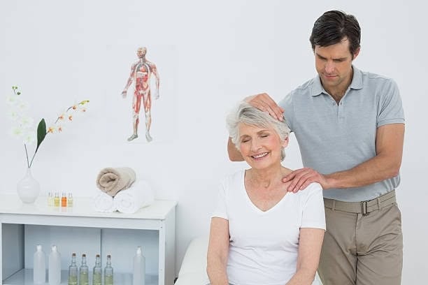 A chiropractor gently stretches the neck of a smiling senior woman during a treatment session in a medical office