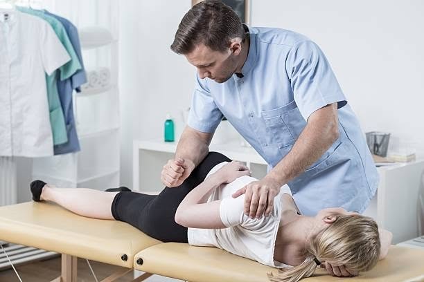 Physical therapist performing a manual hip or lower back adjustment on a patient lying on a treatment table
