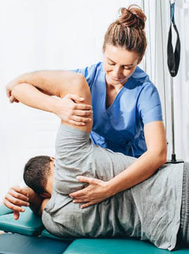 Physical therapist in blue scrubs performing a spinal manipulation on a patient lying on a treatment table